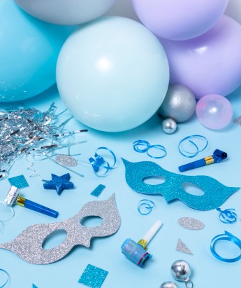 na stole leżą elementy dekoracyjne : maski, balony, wstążki