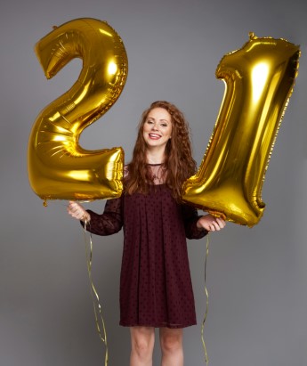 dziewczyna trzymająca w rękach foliowe balony cyfry złote 2 i 1